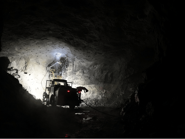 Heavy drilling machinery operating inside a dark underground mine.